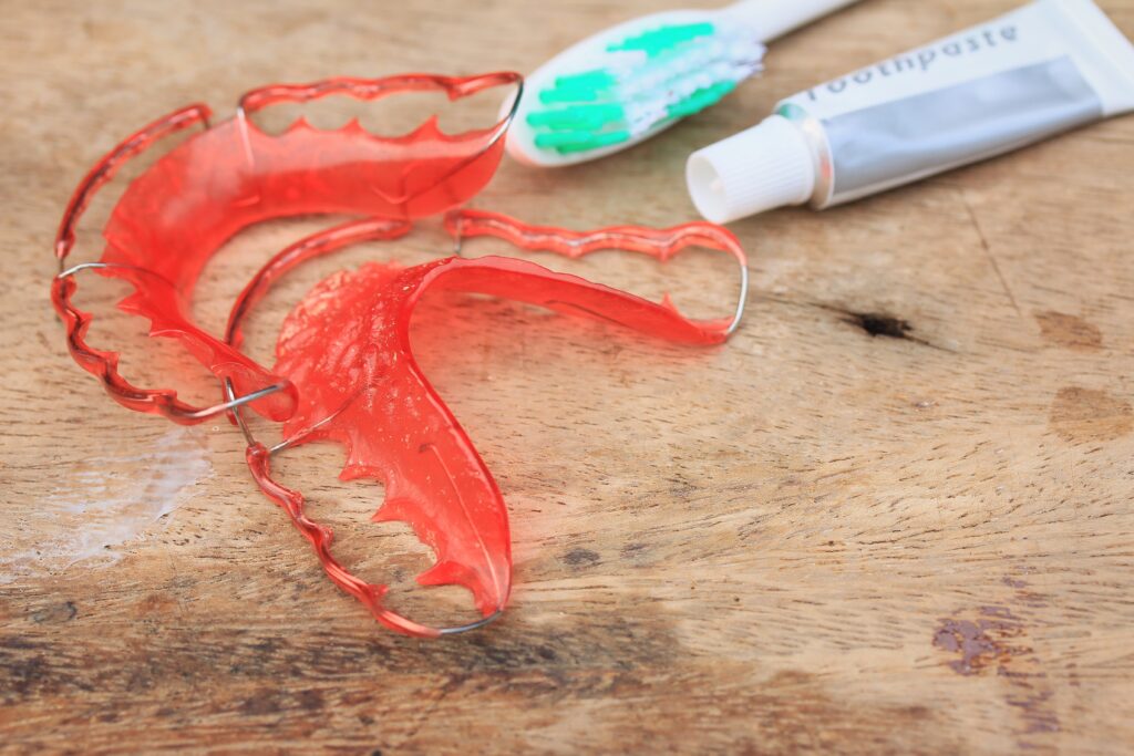 Retainer After Braces. red wire retainer with toothpaste and a toothbrush